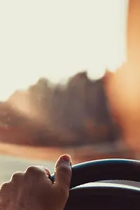 Man driving car, hand on steering wheel, looking at the road ahead,sunset.